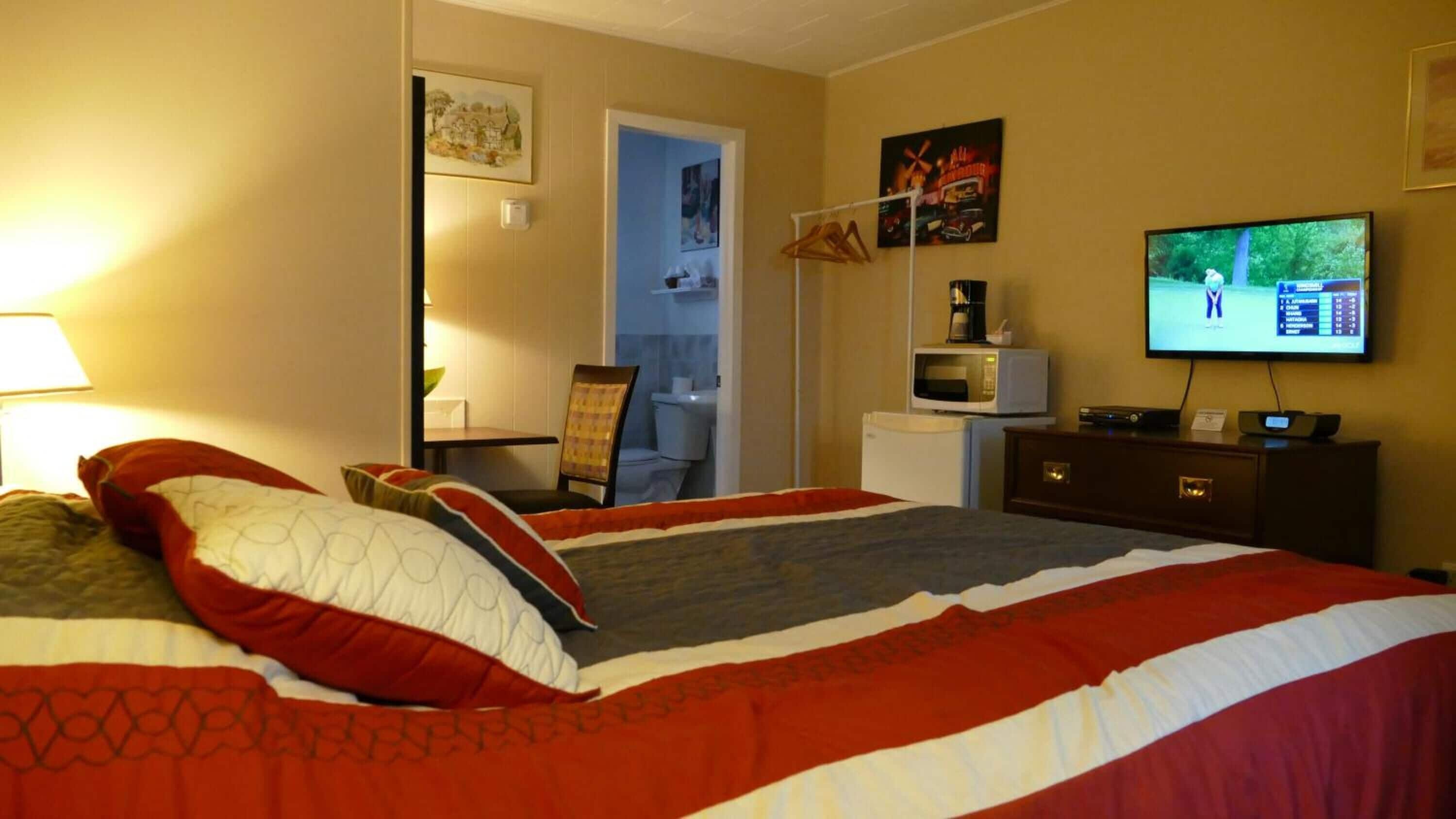 Una habitación de hotel con una cama grande, televisor, escritorio con silla y microondas.