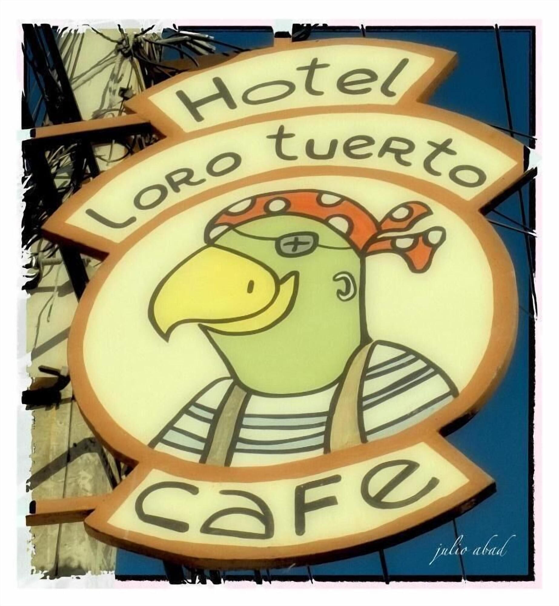 Une enseigne représentant un oiseau de dessin animé portant un bandana et un chapeau, sur laquelle on peut lire les mots « Hotel Loro tuerto cafe ».