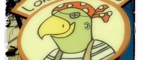 Une enseigne représentant un oiseau de dessin animé portant un bandana et un chapeau, sur laquelle on peut lire les mots « Hotel Loro tuerto cafe ».