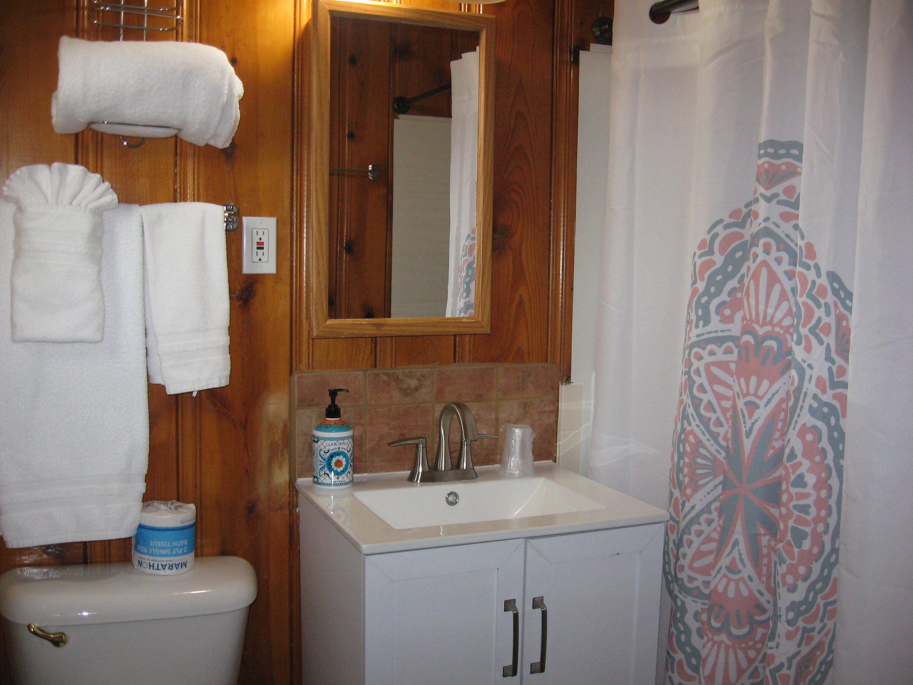 A bathroom with a toilet, sink, and mirror. There are towels hanging on the wall and a shower curtain with a floral pattern.