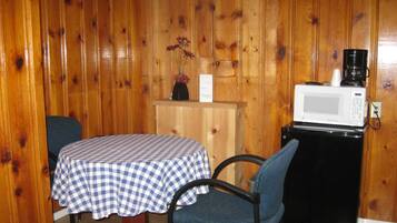 A small wooden room with a checkered table, a single chair, a microwave, and a coffee maker on a counter.