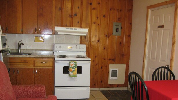 A compact kitchen with wooden cabinets, a white stove, and a dining area with a red table and black chairs. - Masters Inn (Soap Lake)