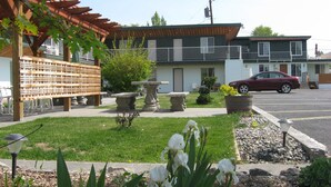 Ein Wohngebäude mit Balkon, Parkplatz und Gartenanlage mit Pflanzen und Bank.