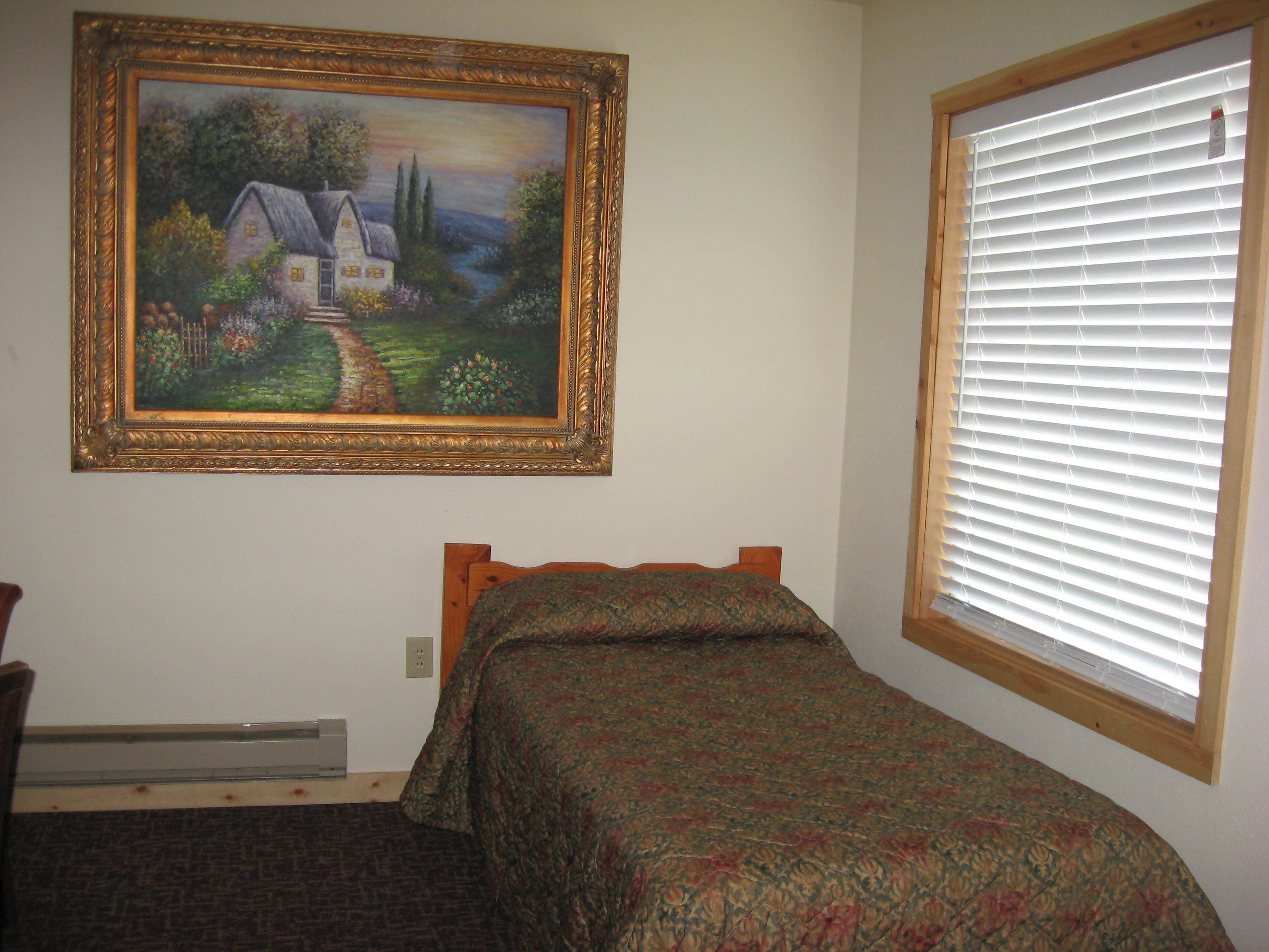 A bedroom with a bed, a painting on the wall, and a window with blinds.