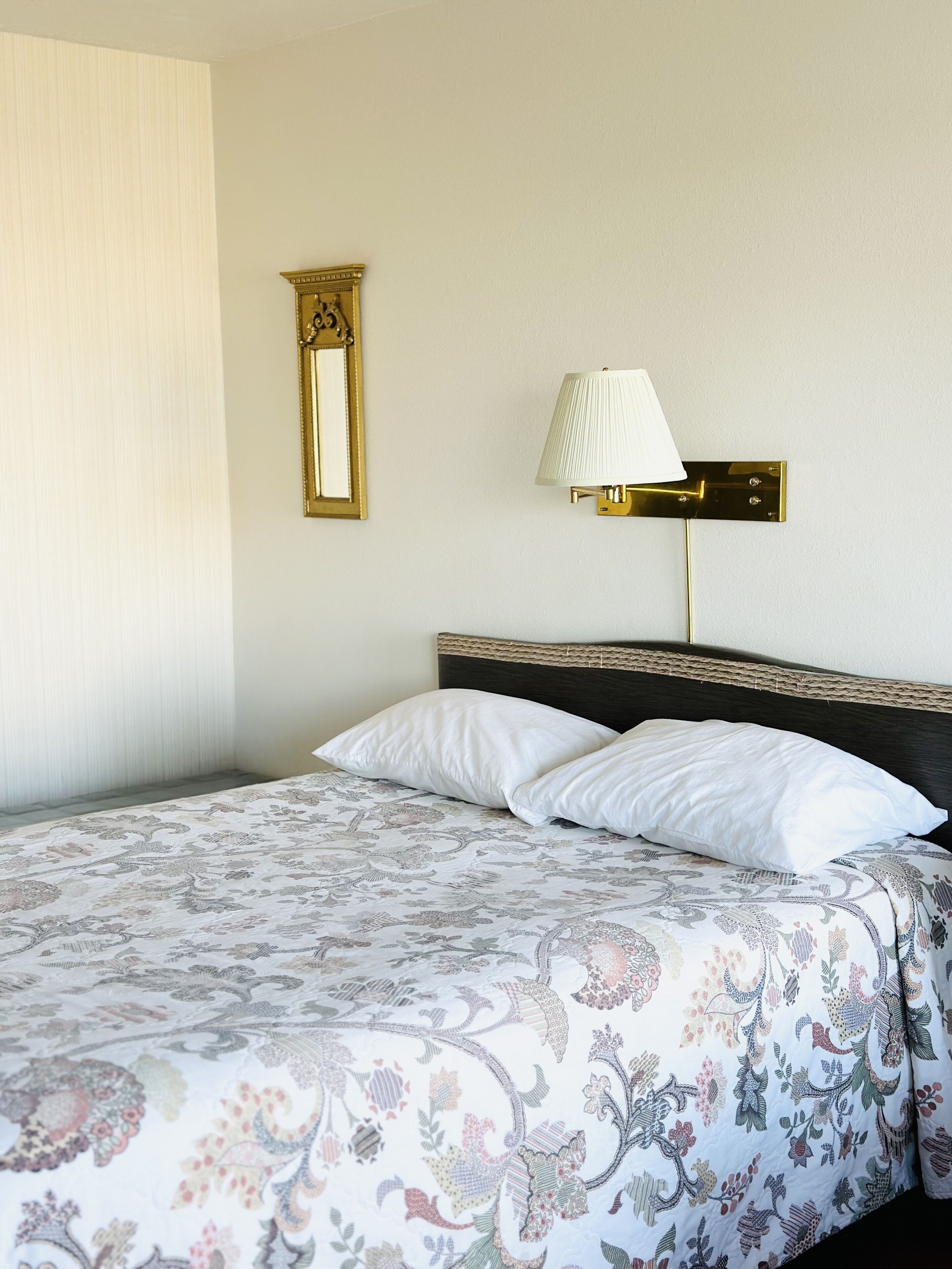 A hotel room with a bed, a wall-mounted lamp, and a mirror.