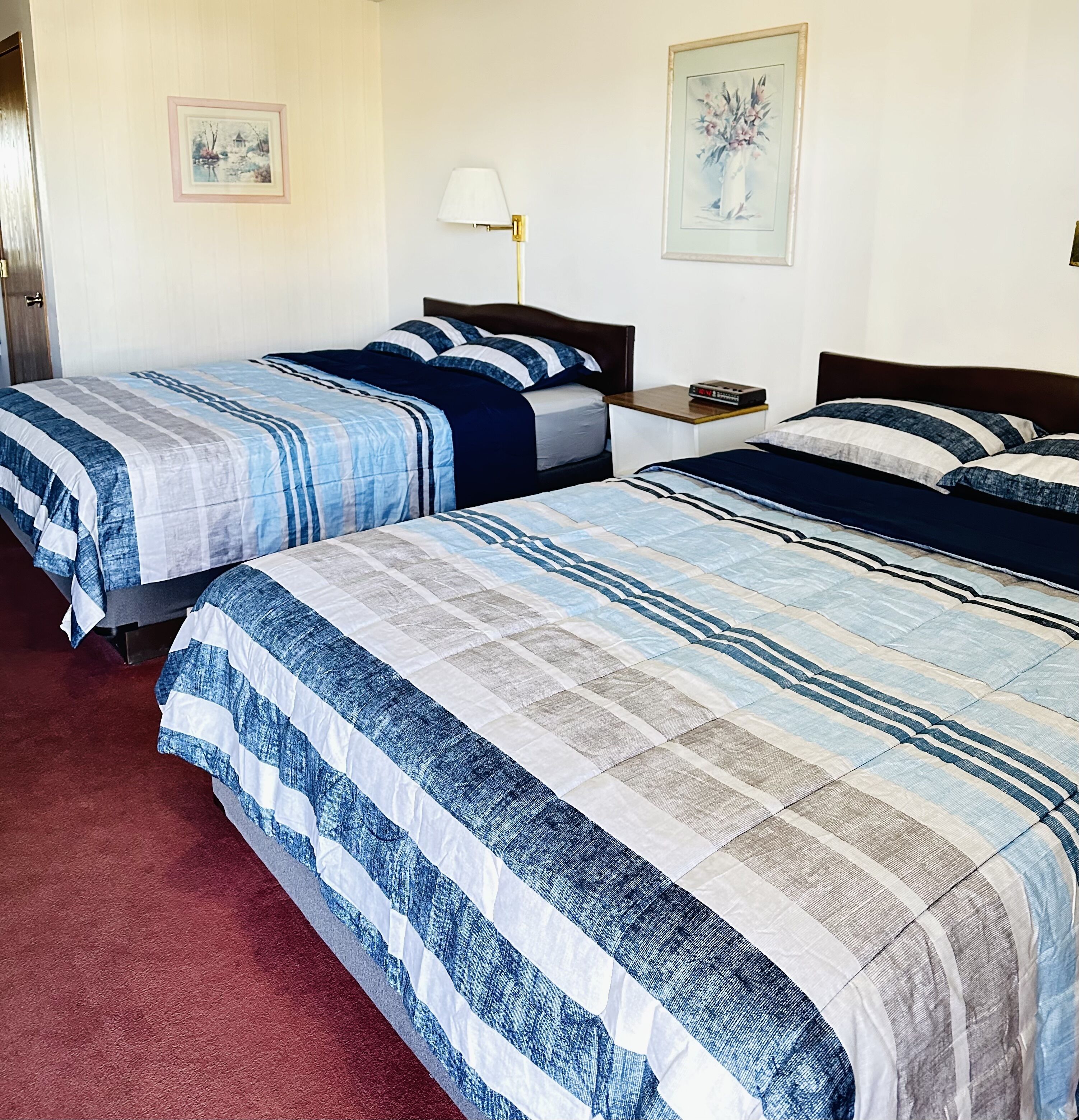 Une chambre d’hôtel avec deux lits, chacun doté de draps à rayures, une table de chevet avec une lampe et un tableau encadré au mur.