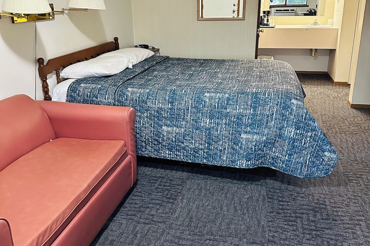 Ein Hotelzimmer mit Bett, einem roten Sofa, einem Badezimmer mit Spiegel und einer Wandlampe.
