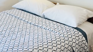 Un lit recouvert d’une couvre-lit à motifs, une lampe fixée au mur et un tableau encadré représentant un paysage marin.