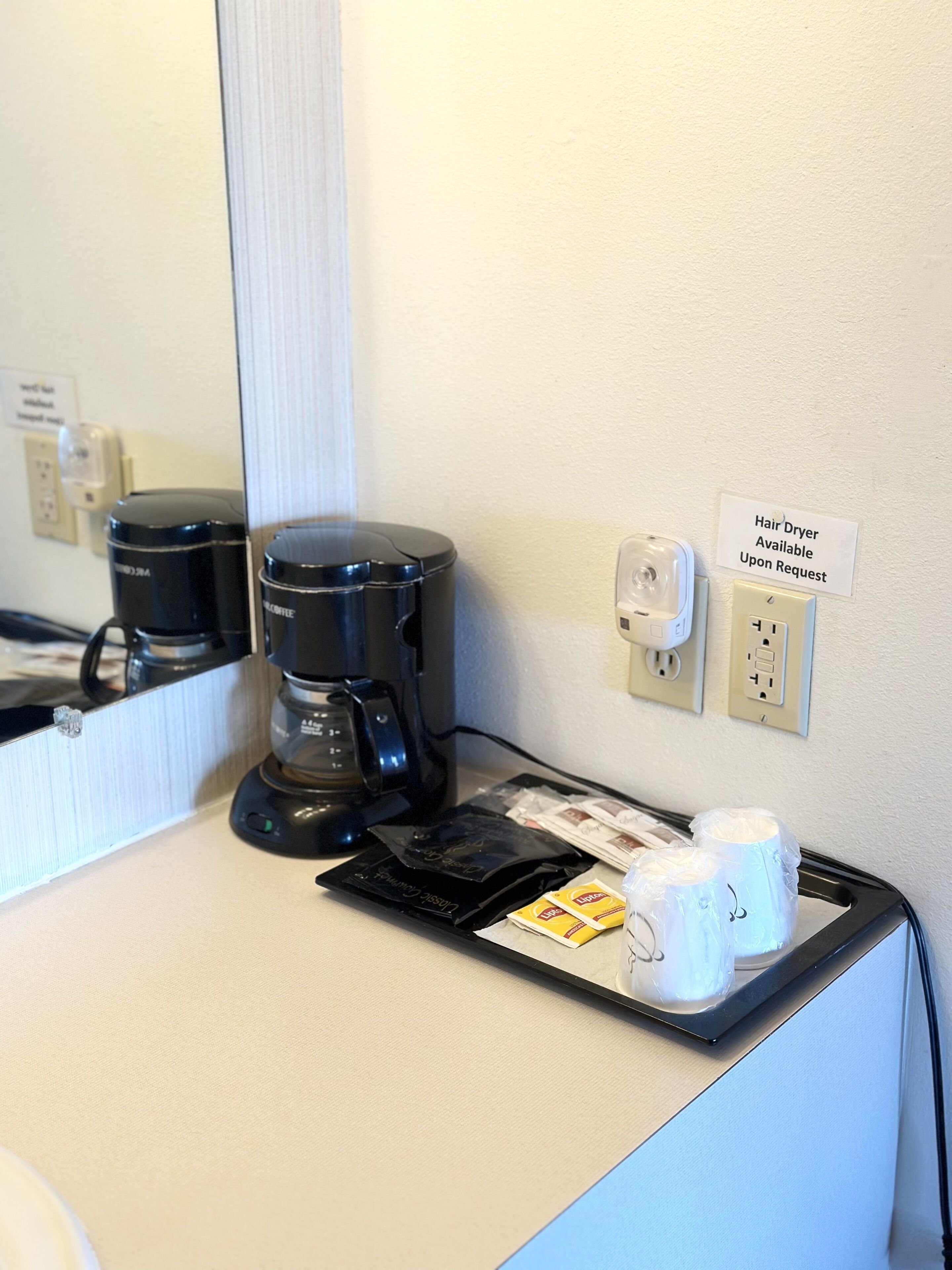 Ein Hotelzimmer mit Kaffeemaschine, einem Hinweis zum Föhn und Toilettenartikeln auf der Ablagefläche.