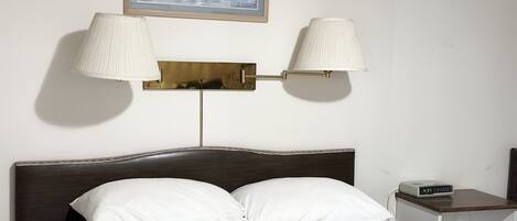 A neatly made bed with a floral bedspread, two bedside lamps, a clock, and a framed picture on the wall.