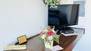 Un bureau en bois avec une télévision, une plante, un panneau indiquant un espace non-fumeur, une télécommande et une petite lampe de bureau.