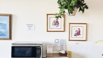 A microwave oven, a framed picture, a sign, and a plant on a wall.