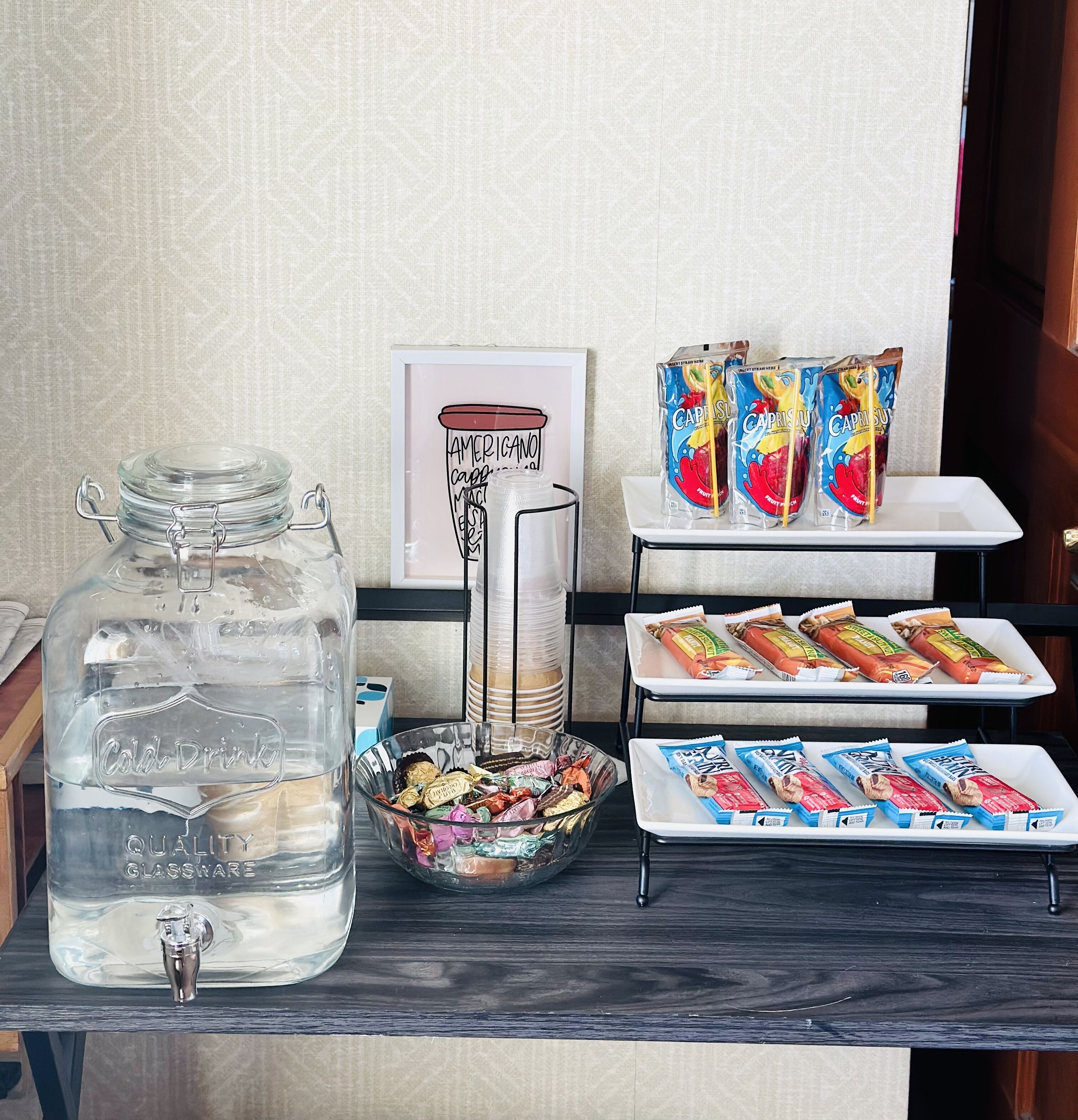 Un coin collation comprenant un bocal en verre étiqueté « Verres de qualité pour boissons fraîches », un bol rempli de bonbons variés et deux plateaux de boissons aux fruits CapriSun.