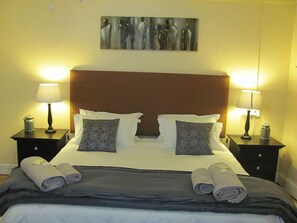 A neatly made bed with a brown headboard, two bedside lamps, and a painting above.