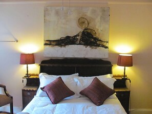 Un dormitorio con una cama, dos lámparas de noche, un cabecero y una obra de arte colgada en la pared.