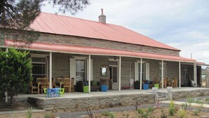 Un bâtiment en pierre avec un toit rouge, un espace extérieur aménagé pour s’asseoir et un jardin avec différentes espèces de plantes.