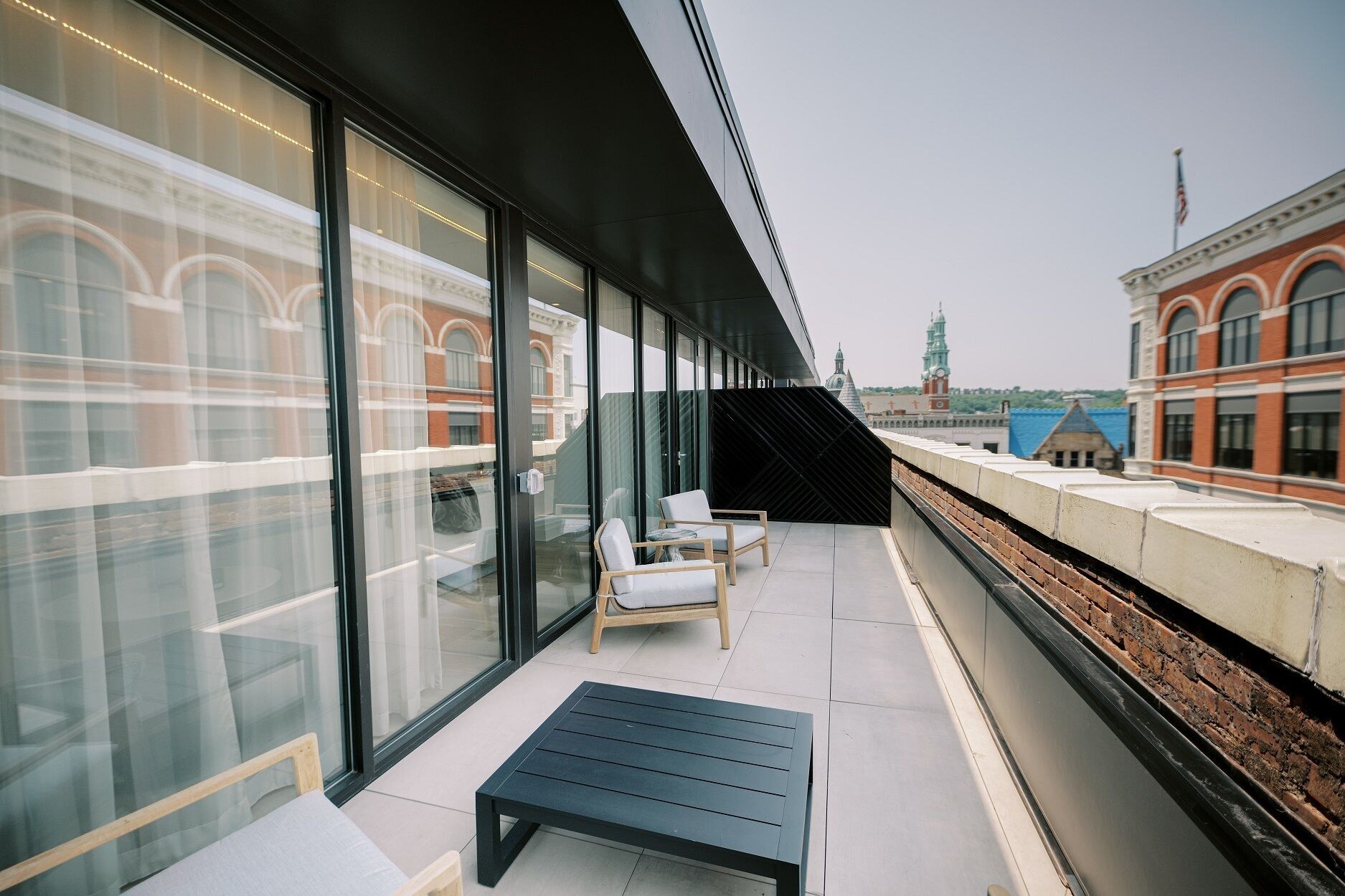 A modern outdoor seating area with glass walls, a bench, and a view of a historic building and a bridge.