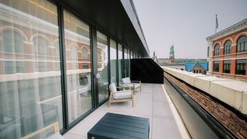 Una zona de estar al aire libre con diseño moderno, paredes de vidrio, un banco y vistas a un edificio histórico y un puente.