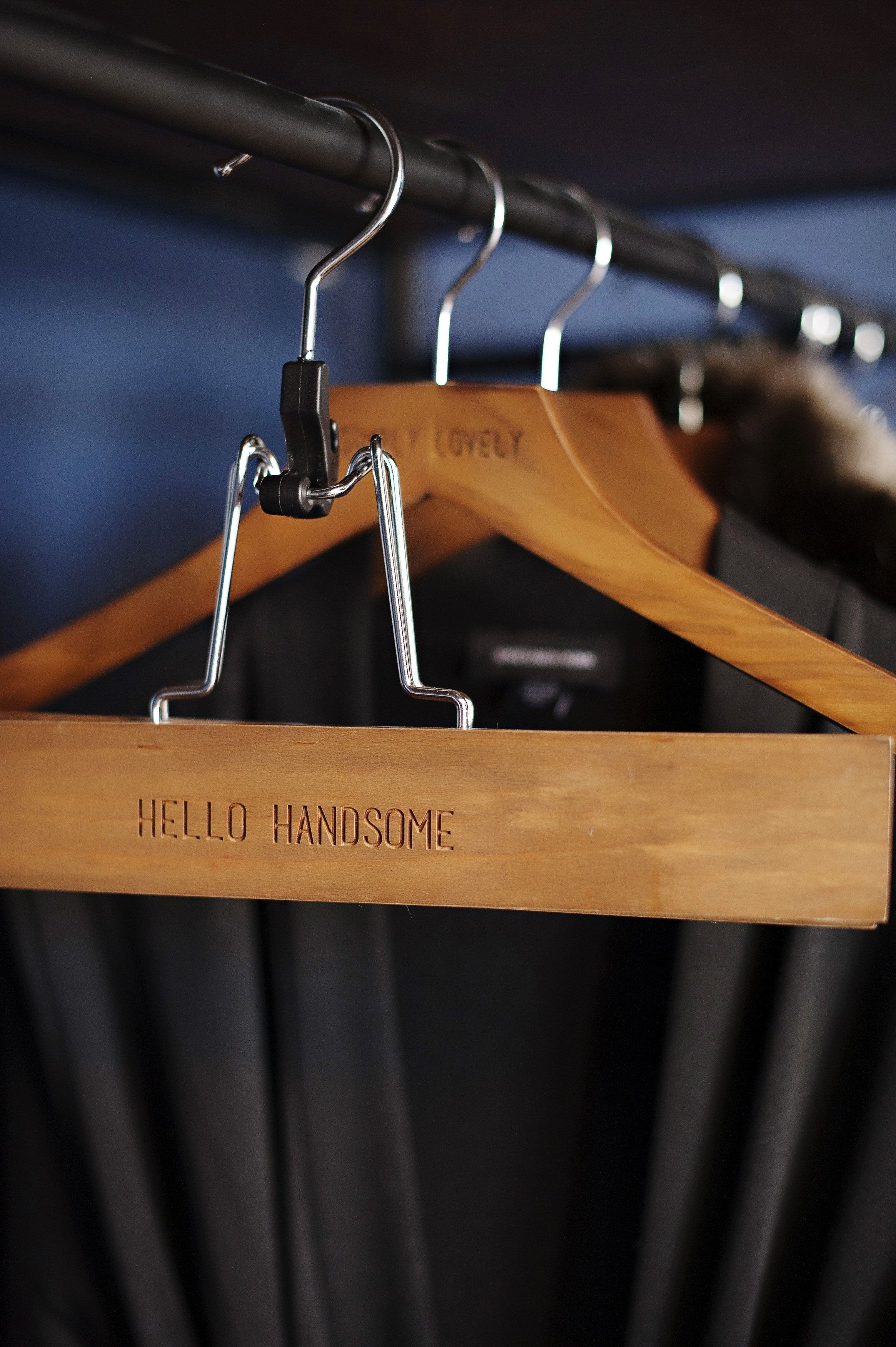 A wooden hanger with the text "HELLO HANDSOME" hanging on a metal rack.