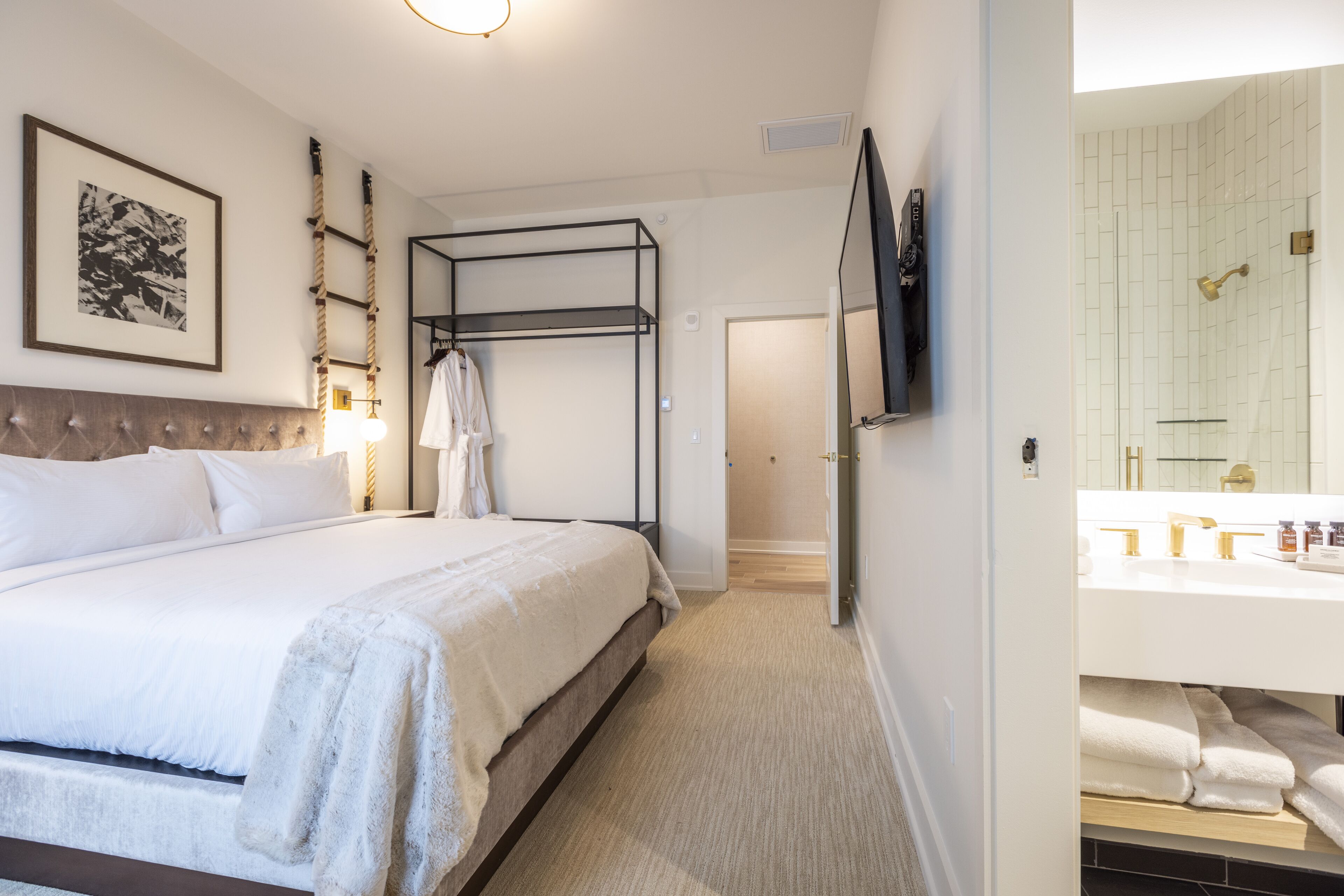 A hotel room with a bed, a bunk bed, a bathroom with a sink and mirror, and a framed picture on the wall.