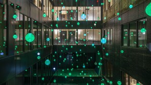 A modern building with multiple floors, large windows, and a central open space with hanging green lights.