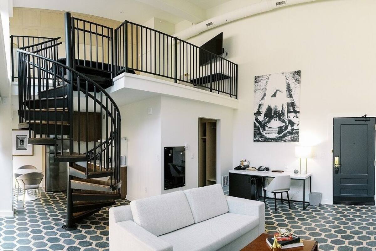 A spacious living area with a modern staircase, a sofa, a dining table, and artwork on the walls.