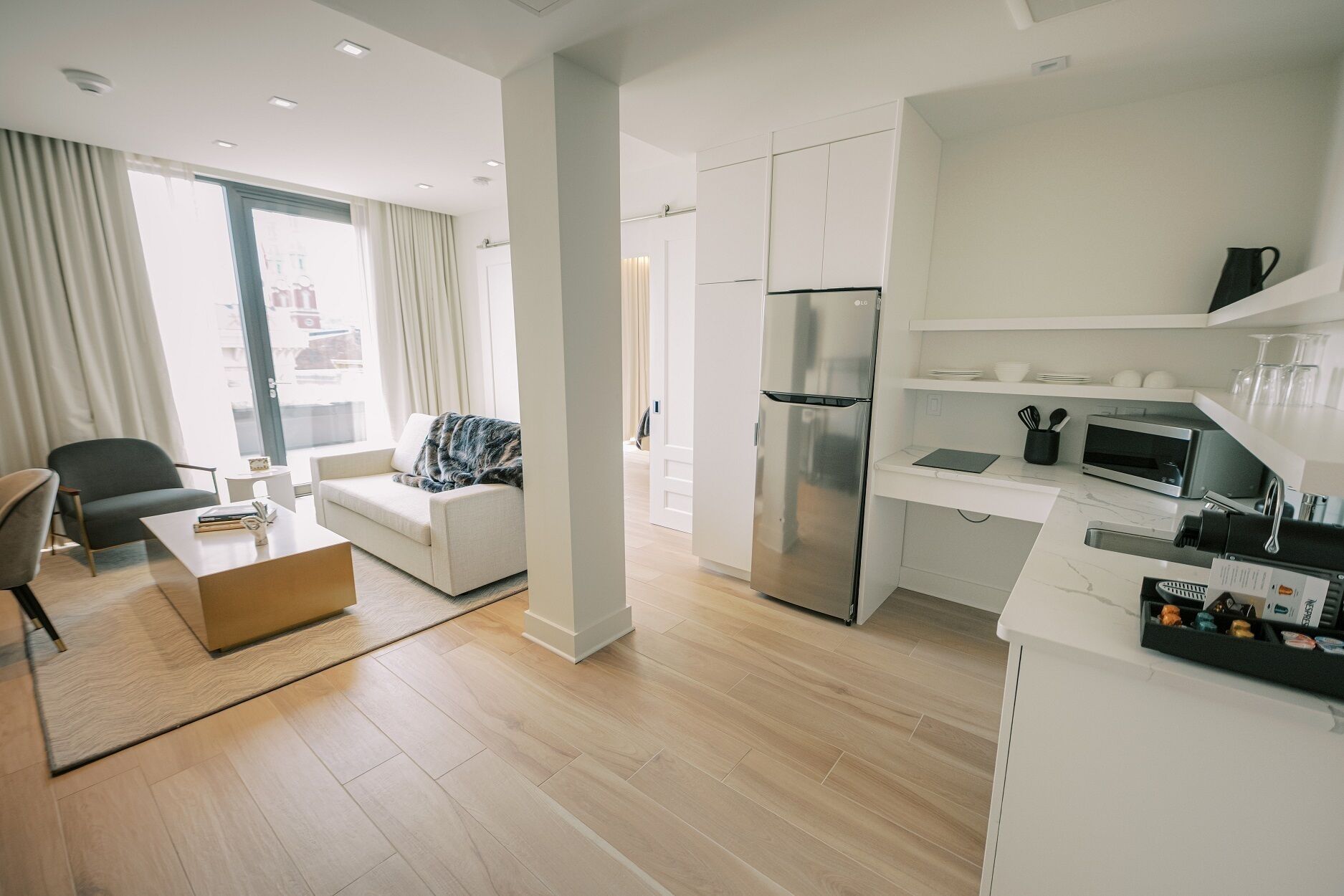 A modern apartment with a living area, kitchenette, and a large window with curtains.