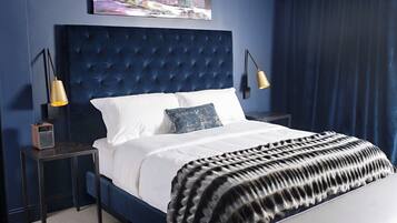 A bedroom with a tufted headboard, white bedding, a black and white throw blanket, and two bedside lamps.