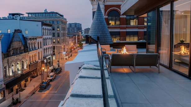 A rooftop terrace with outdoor seating, overlooking a cityscape with historic buildings and a modern structure.