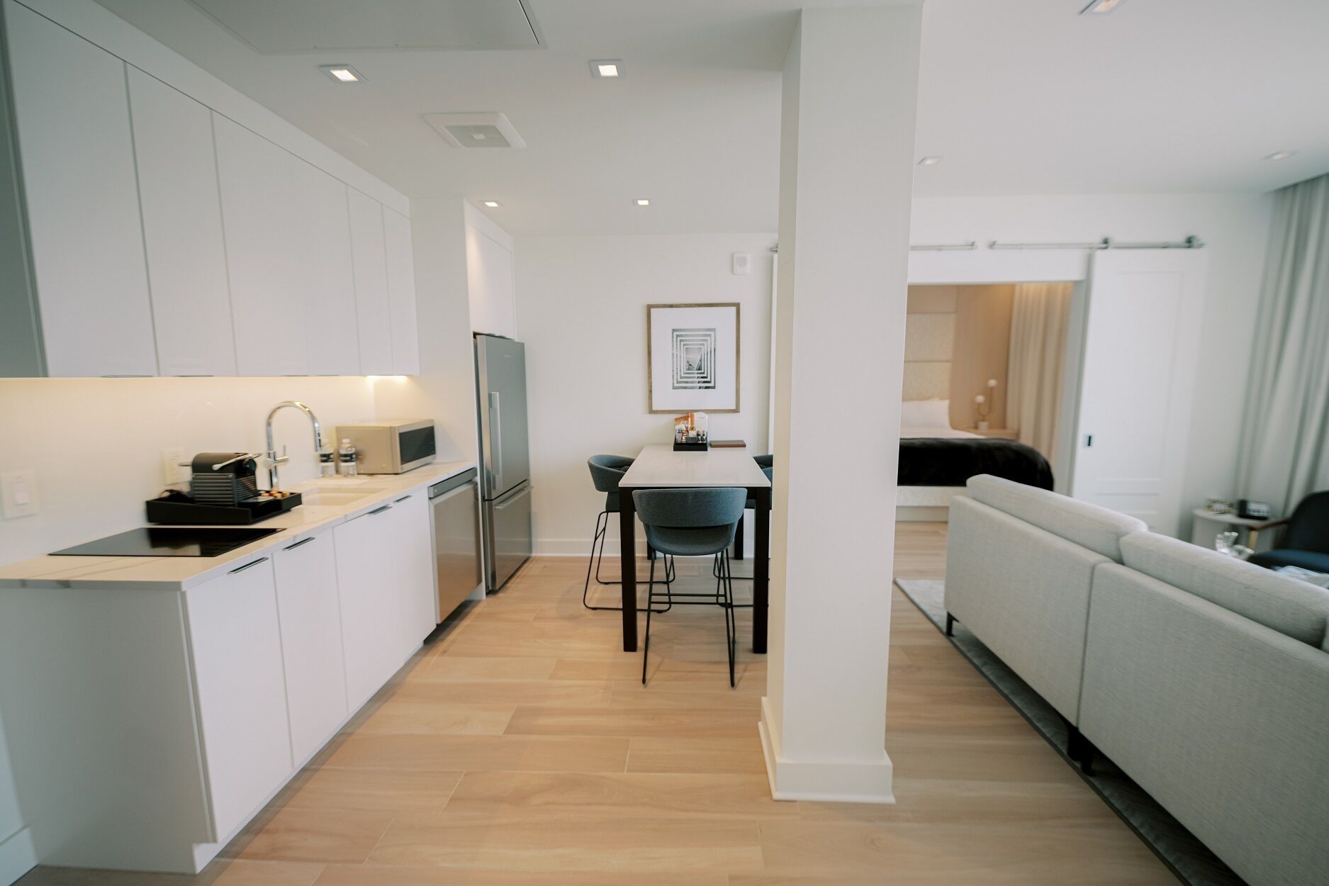 A modern kitchen with white cabinets, a dining area with a table and chairs, and a living area with a sofa.