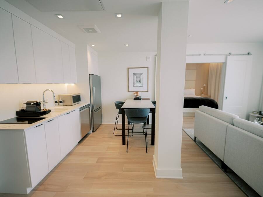 A modern kitchen with white cabinets, a dining area with a table and chairs, and a living area with a sofa.