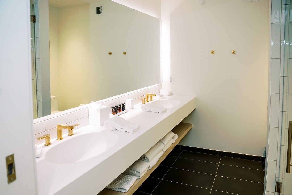 A modern bathroom with a white vanity, two sinks, gold faucets, and a large mirror.