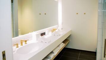A modern bathroom with a white vanity, two sinks, gold faucets, and a large mirror.