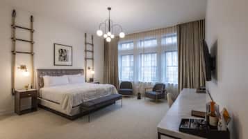 Habitación de hotel con cama, escritorio, silla, televisor y ventana con cortinas.