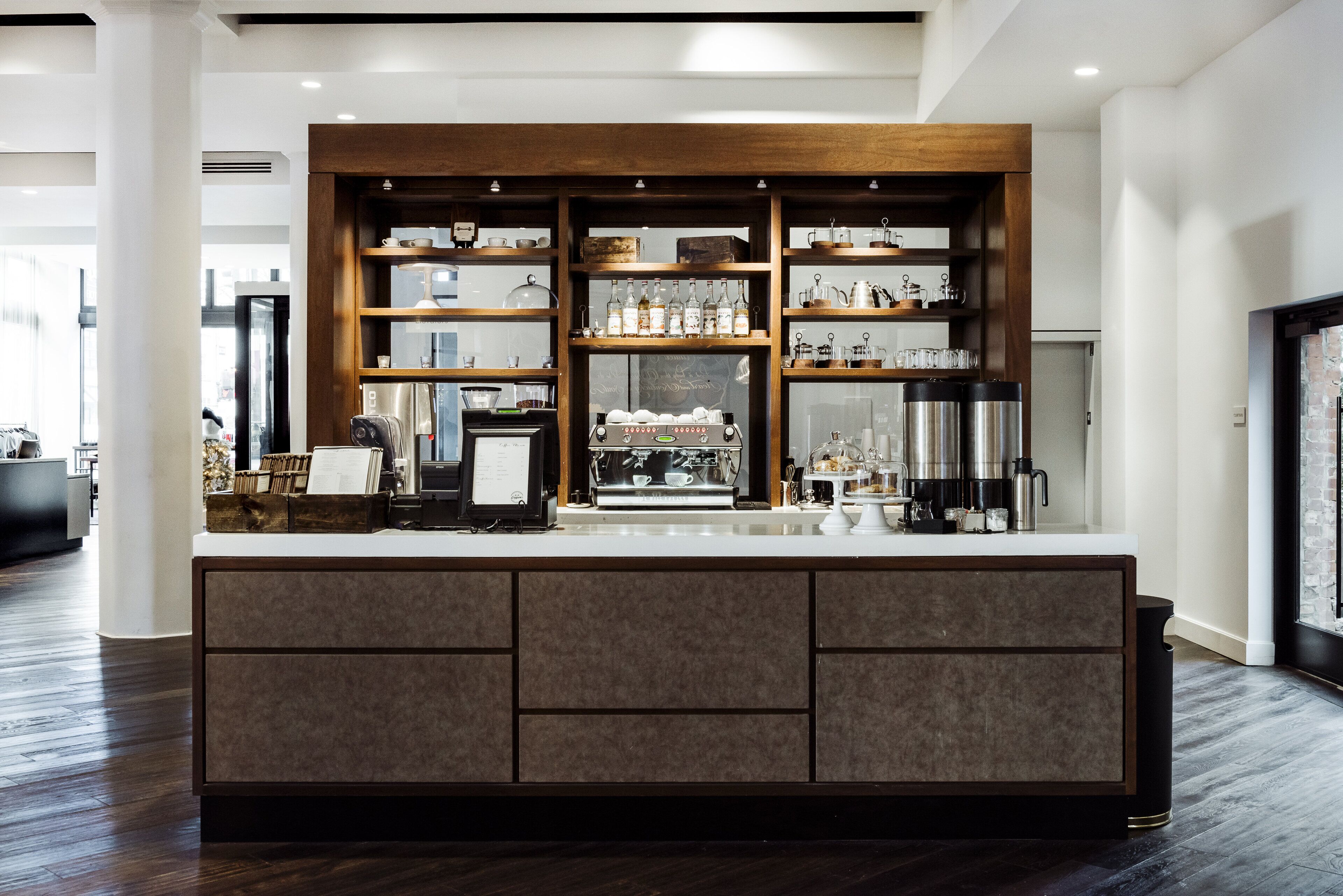 Un espace bar moderne doté d’un comptoir central, d’étagères où sont rangés les verres et d’une machine à café.