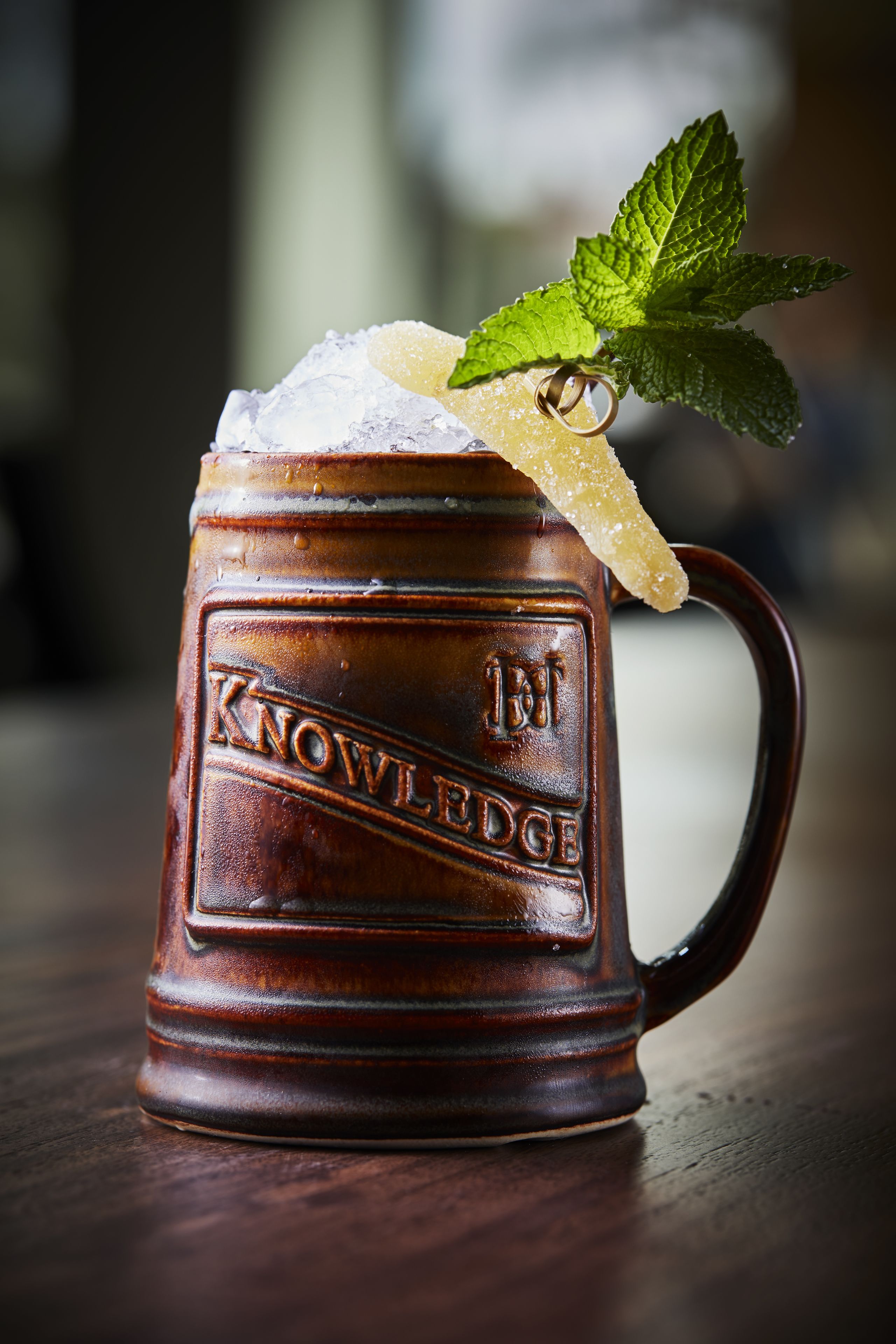 Una taza de madera con la palabra 'KNOWLEDGE' en relieve, llena de una bebida, azúcar y una hoja de menta.