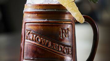 Una taza de madera con la palabra 'KNOWLEDGE' en relieve, llena de una bebida, azúcar y una hoja de menta.