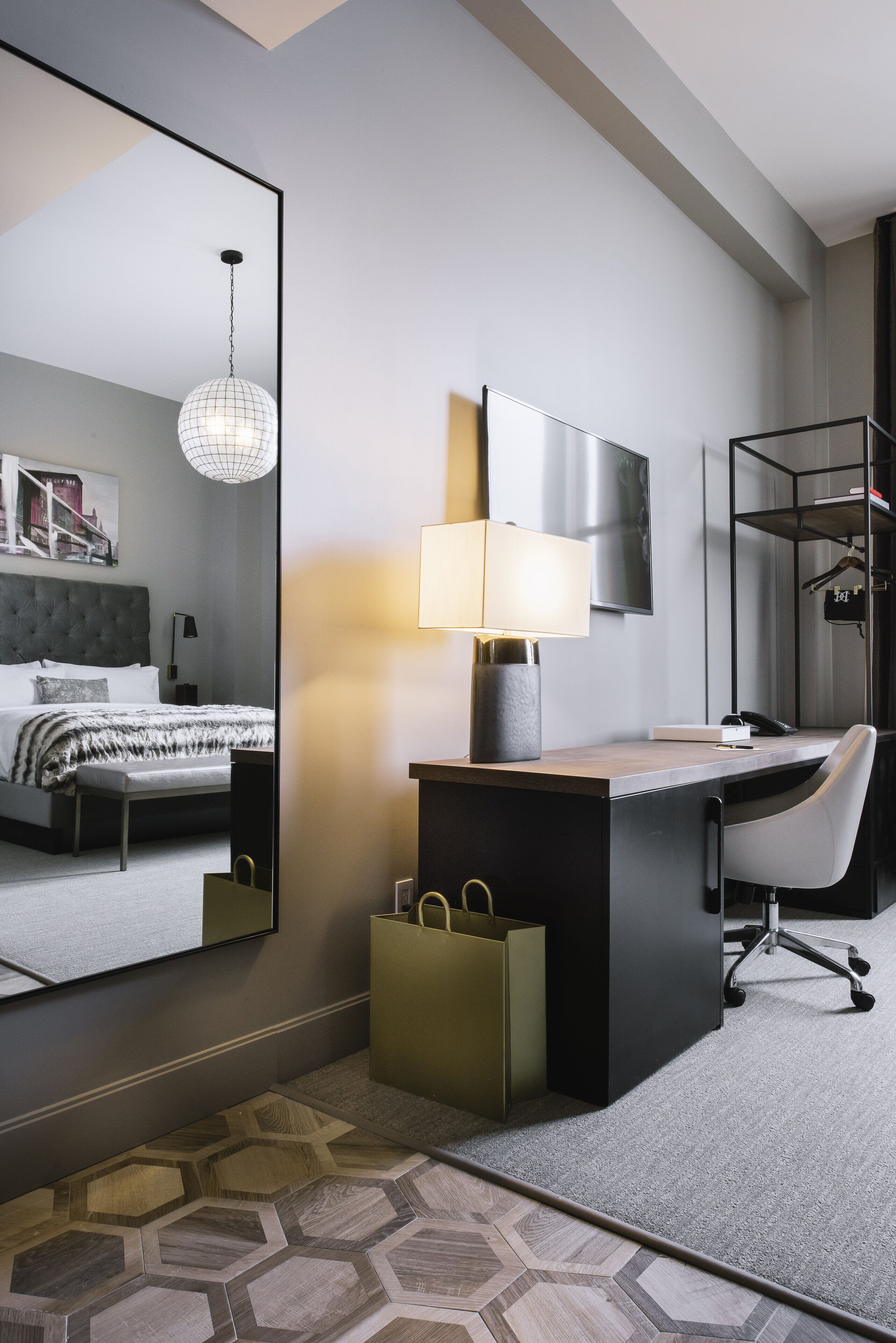 Una habitación de hotel moderna con una cama grande, un escritorio con lámpara, un espejo y un armario.