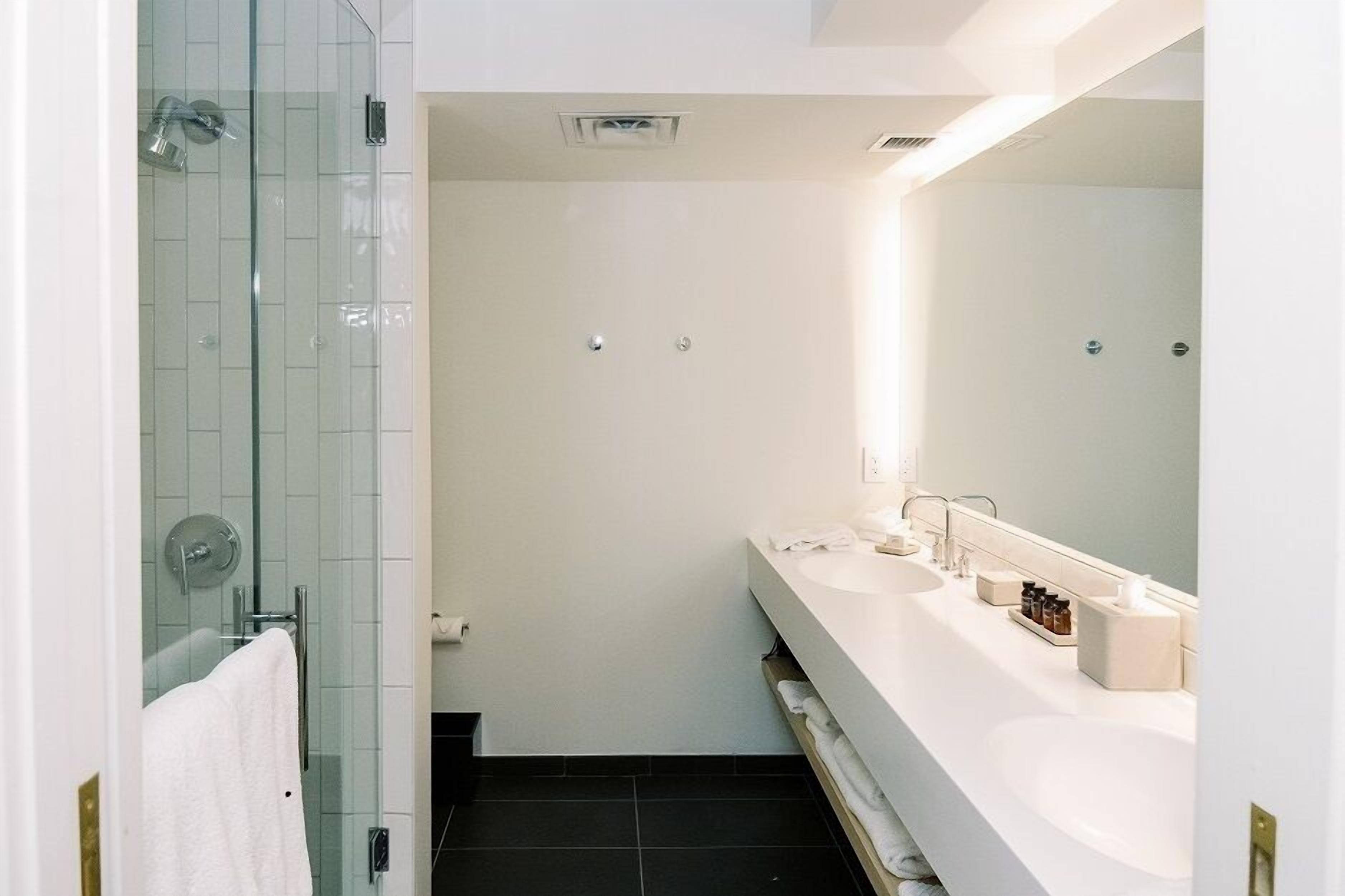 Un baño moderno con ducha de vidrio, un lavamanos blanco y un espejo grande, y piso de baldosas oscuras.