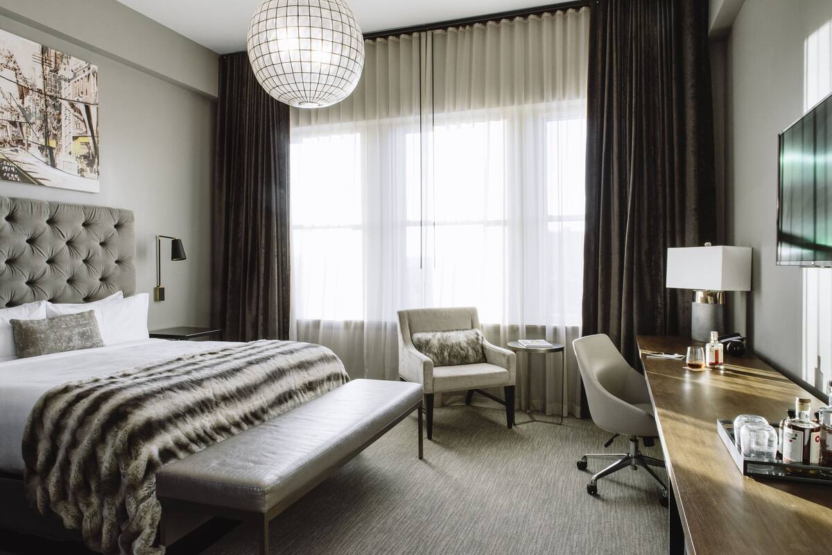 A hotel room with a large bed, a desk, a chair, a small table, and a TV.
