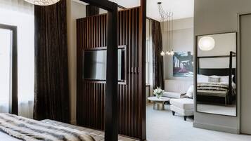 A modern bedroom with a large bed, a TV mounted on a wooden panel, a sofa, a coffee table, and a large mirror.