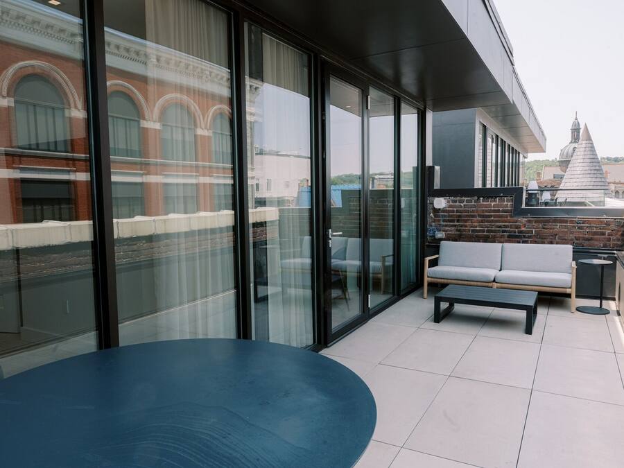 A modern outdoor seating area with a blue table and a grey sofa, large glass windows, and a view of a historic building in the background.