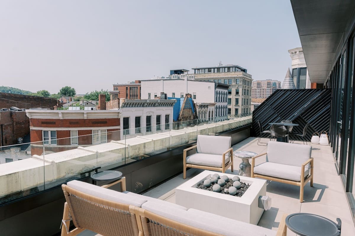 A rooftop terrace with wicker furniture, a fire pit, and a view of the cityscape.