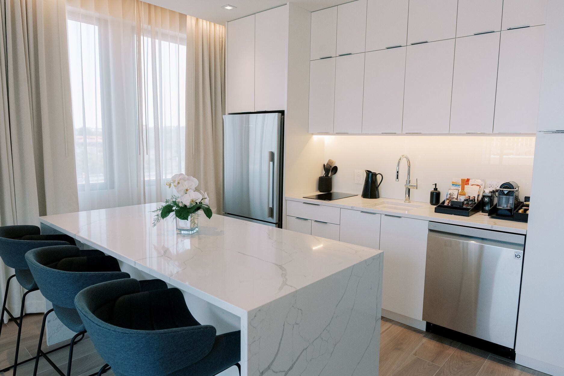 A modern kitchen with white cabinets, a central island with bar stools, and a dining table.
