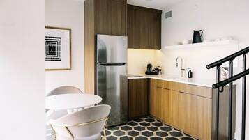 A compact kitchen with a stainless steel refrigerator, wooden cabinets, a white countertop, and a hexagonal patterned floor.