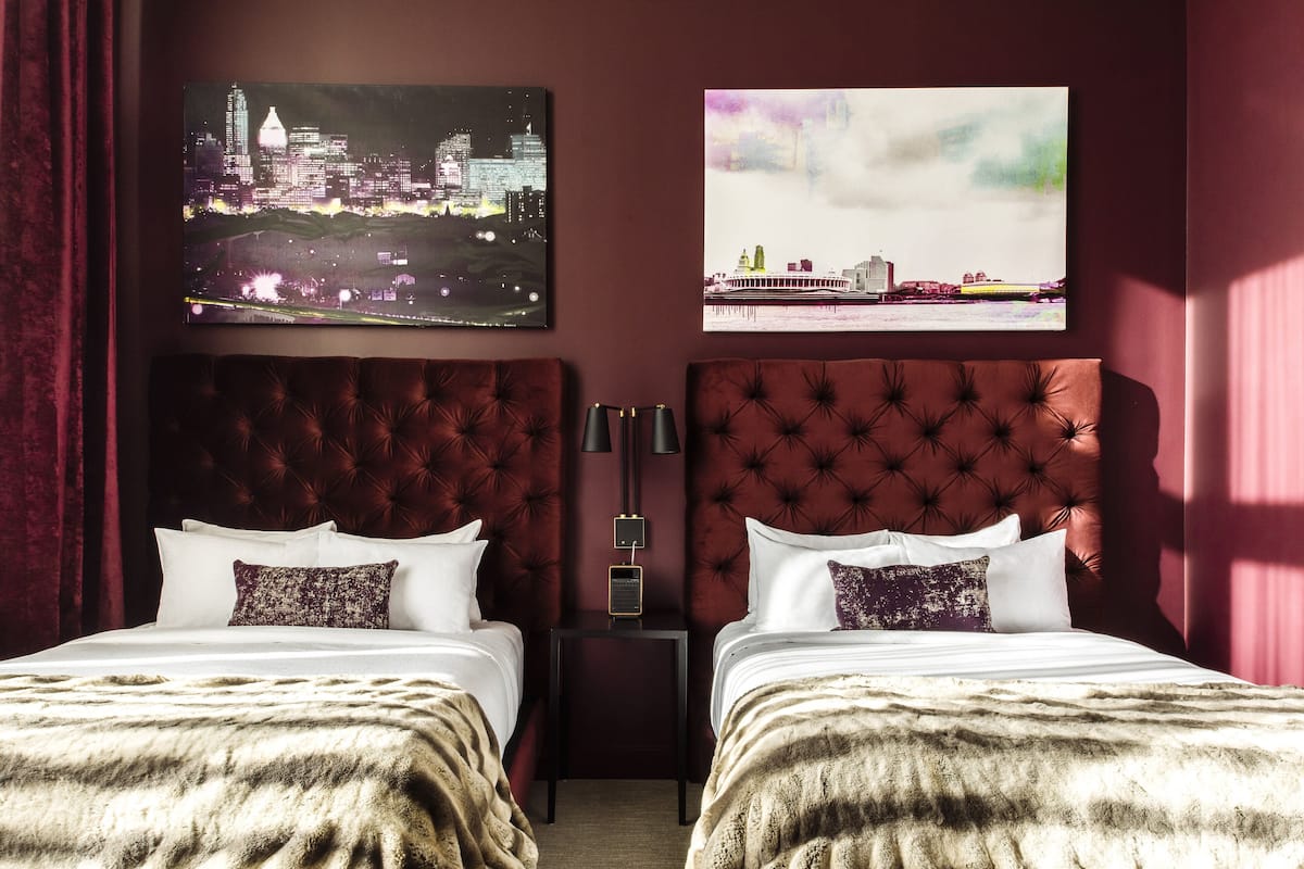 A hotel room with two beds, a nightstand, and two wall-mounted paintings.