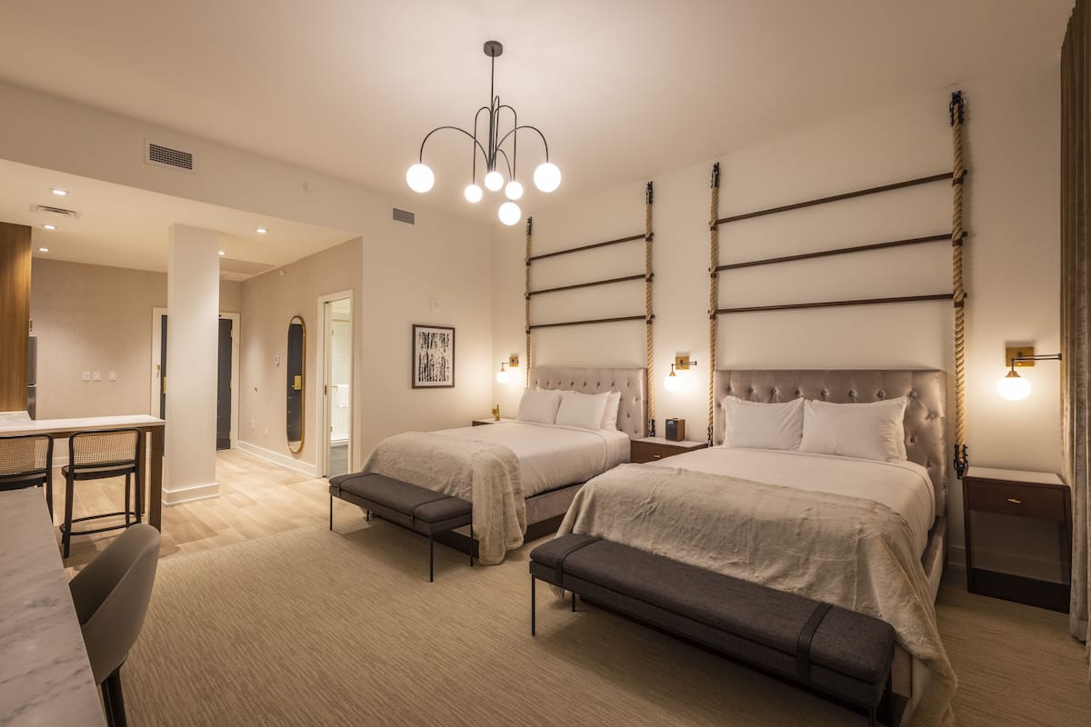A hotel room with two beds, a dining area, and a modern chandelier.