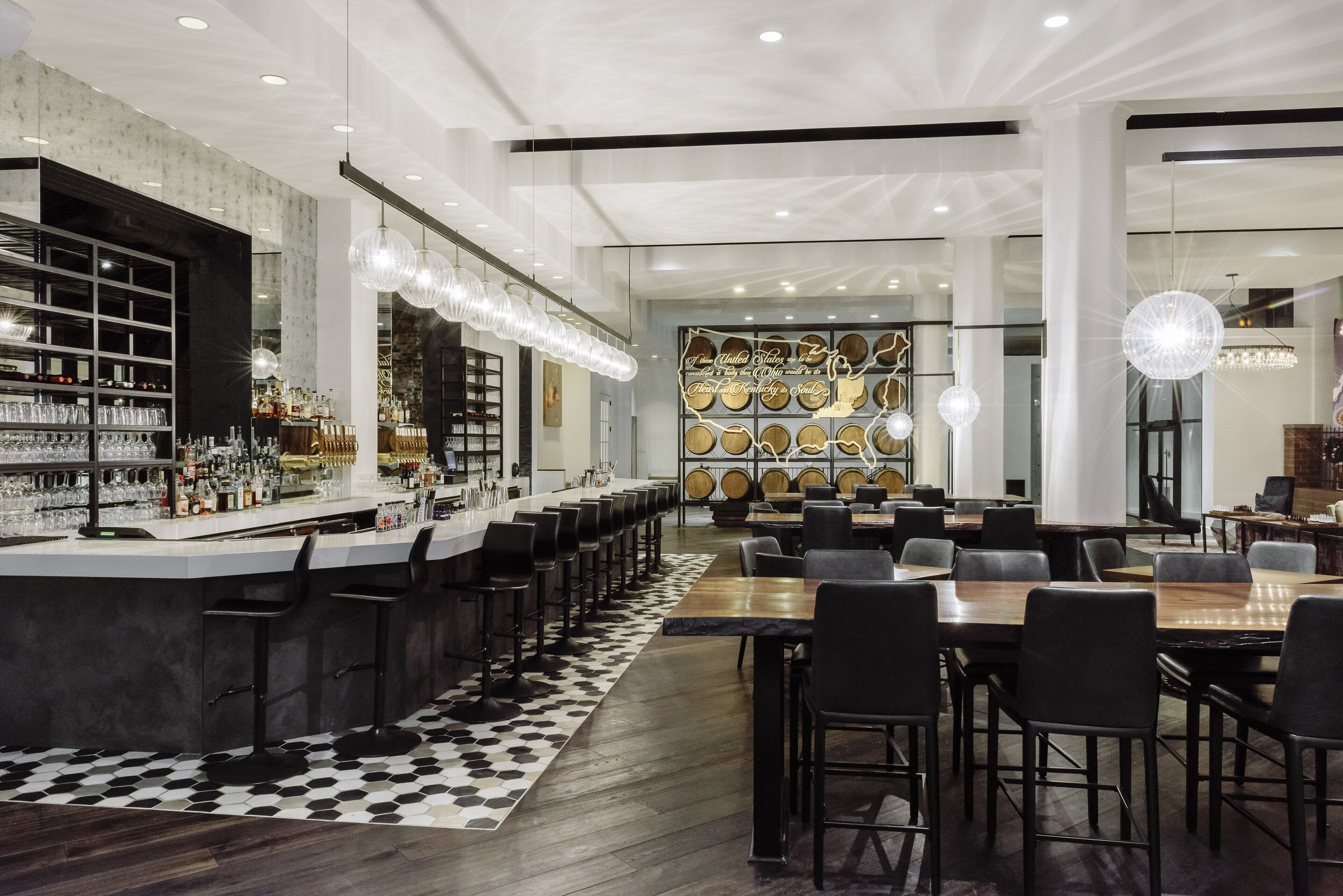 A modern bar area with a long counter, multiple stools, and a patterned rug.