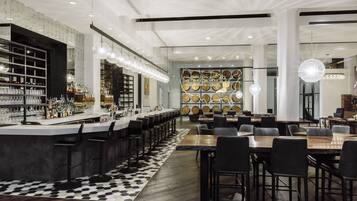 A modern bar area with a long counter, multiple stools, and a patterned rug.