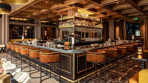 A bar area with a central bar, multiple stools, and shelves stocked with bottles.